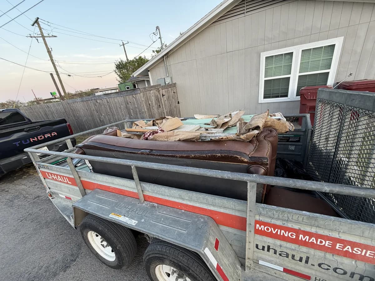 Trailer loaded with a leather sofa and flattened cardboard, parked beside a house